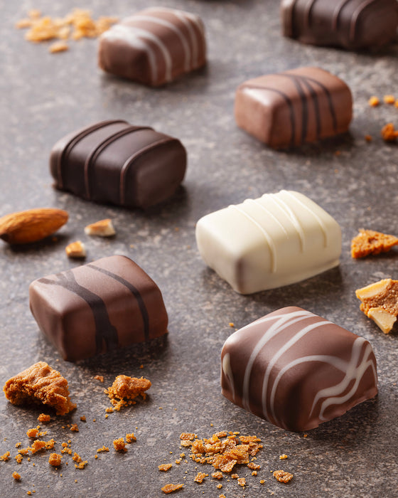 Assorted Leonidas chocolate truffles on a dark surface with crumbs around them.